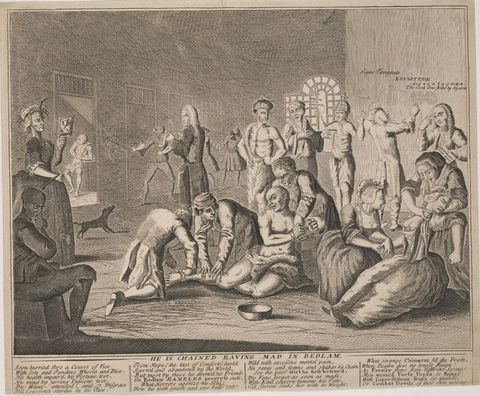Print. Twelve men and three women gather in a shallow space against a deep room lined with cells. At the centre of this group, two men attach a manacle around a third man’s leg. Another man draws gridded globes on a wall to our right.