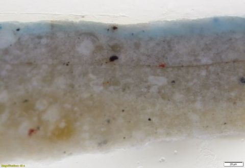 Colour photograph. In this microscopic cross section of paint, layers of grey and white are topped with a layer of pale blue. Text in the lower left corner reads, “Magnification: 40x”, and in the lower right, “20µm”.